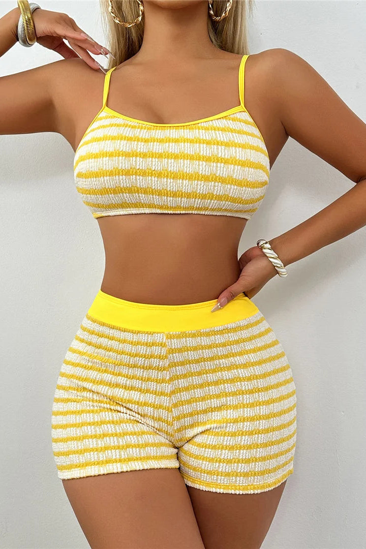 Woman wearing a yellow and white striped bikini and boys shorts outfit on a plain background