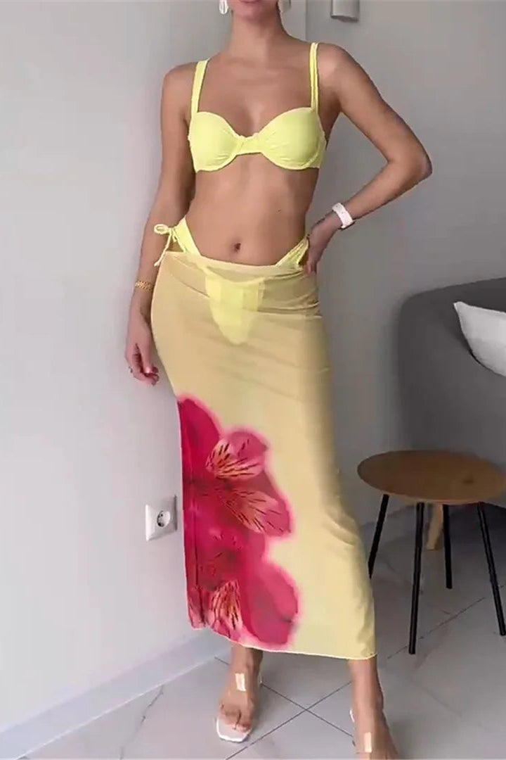 Woman wearing a yellow bikini with a floral skirt in a room.