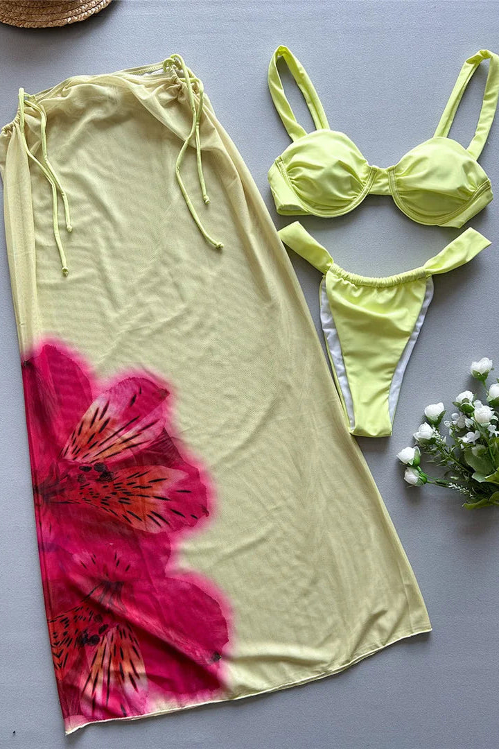 Yellow bikini set with a floral cover-up skirt on a gray surface.