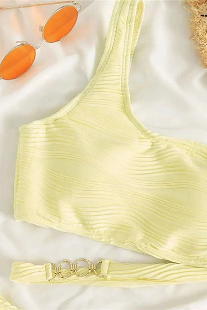 Yellow bikini top with sunglasses and a belt on a light background